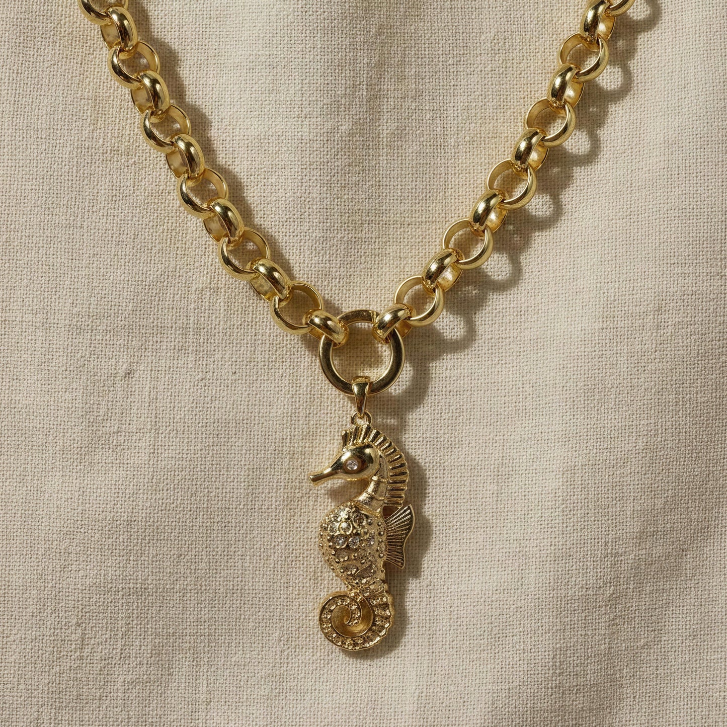 The Seahorse Statement Necklace on a beige fabric background.