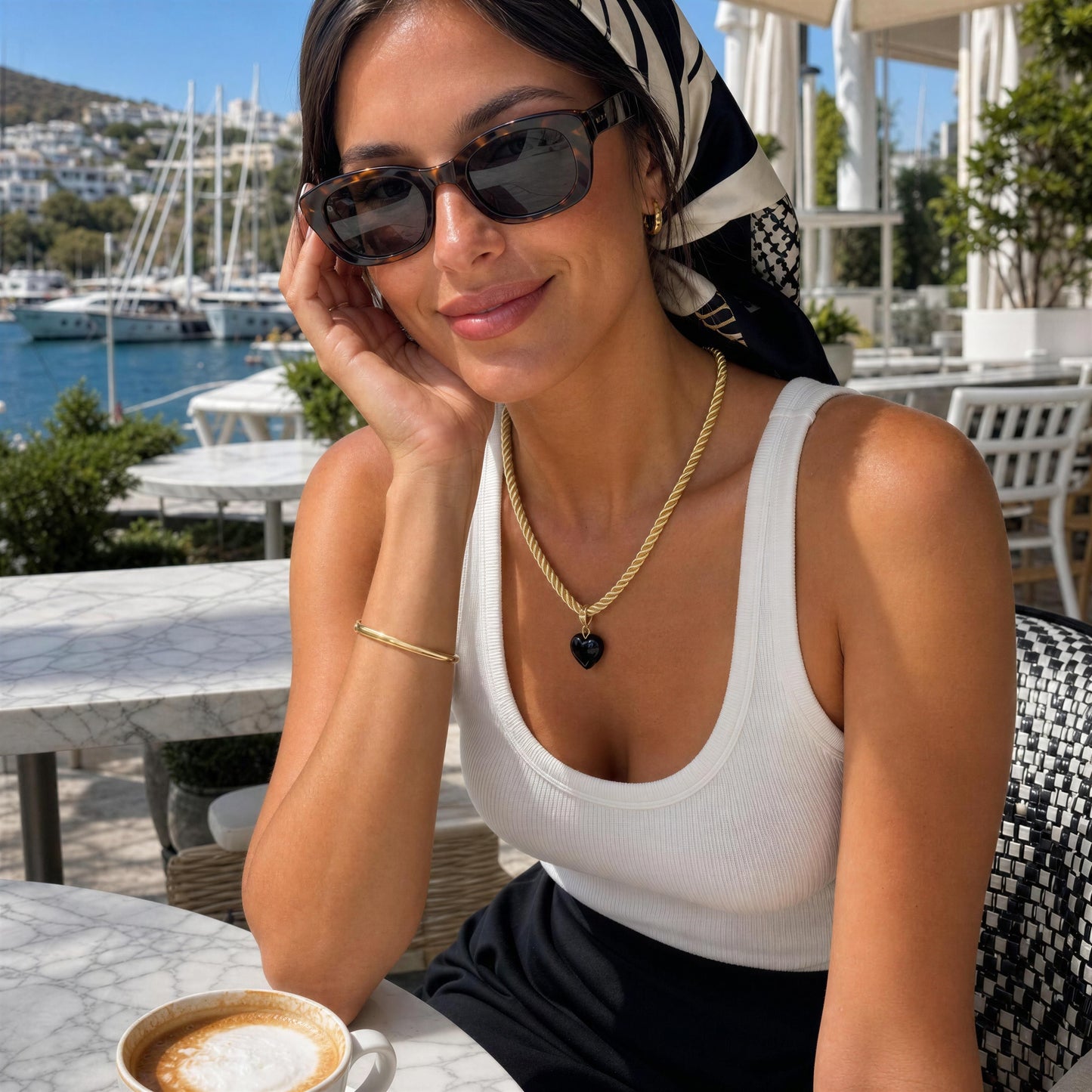 Woman wearing the Siyah Necklace featuring a black Murano glass heart pendant on a twisted gold-tone cord overlooking the Mediterranean coast.