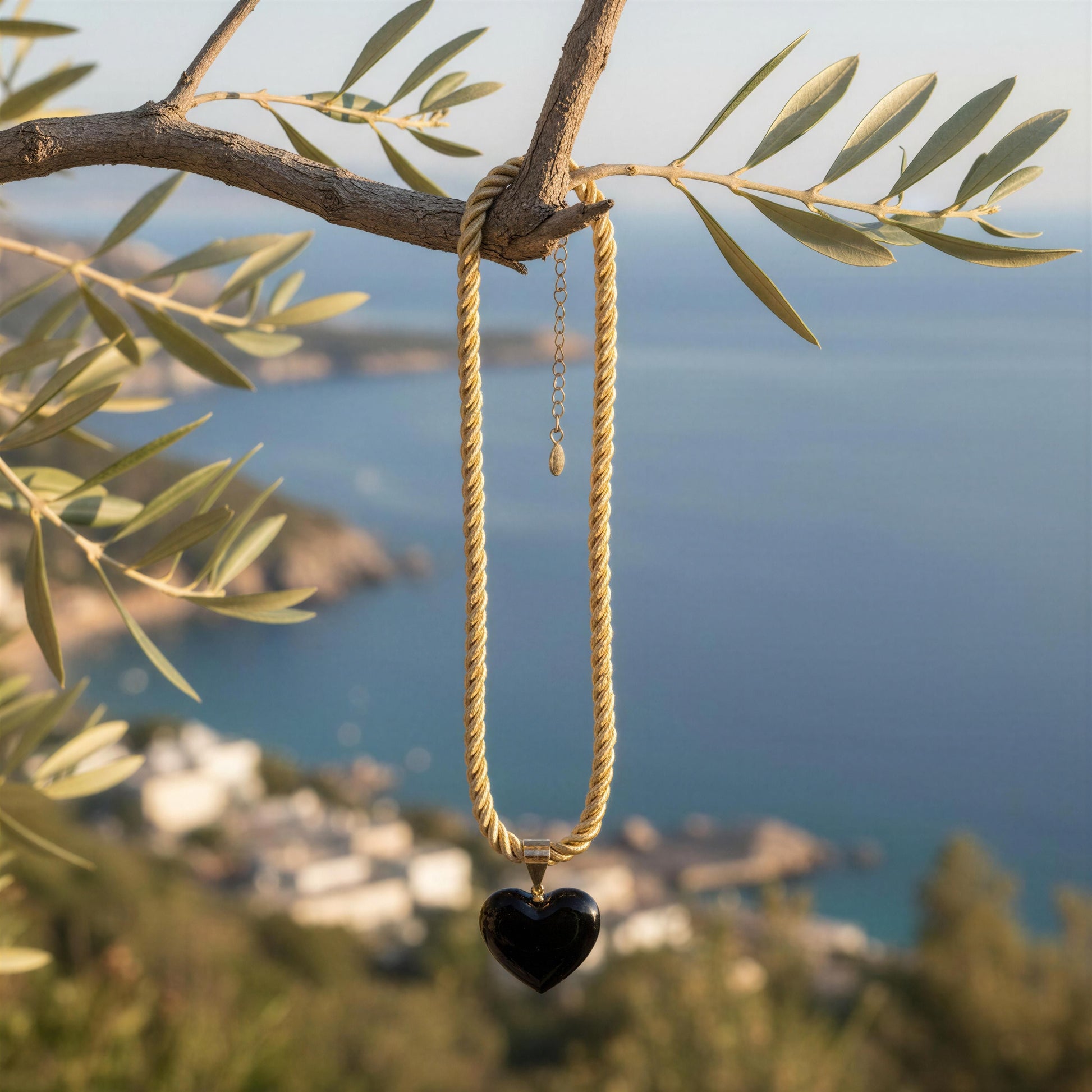 The Siyah black heart necklace from Chica Chica Jewelry with a  twisted gold-tone cord and glossy Murano black heart pendant hanging from tree overlooking the Aegean Sea.