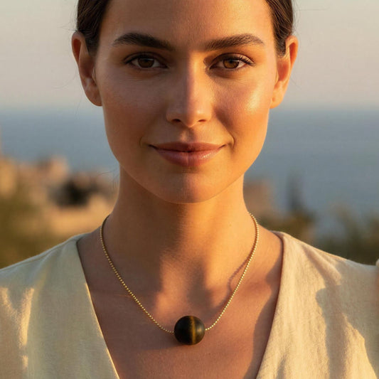 Woman in a light yellow dress standing in front of a scenic background with ocean and buildings wearing the Terra Sol Sphere necklace 