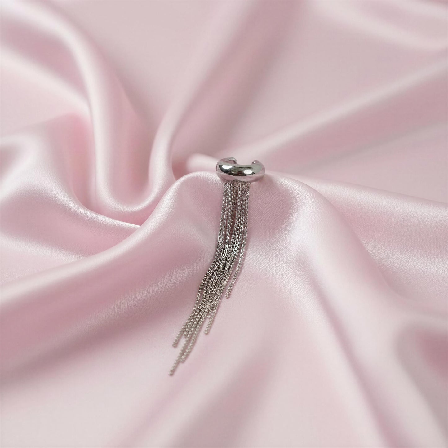 The Vela Silver Ear Cuff on pink satin fabric
