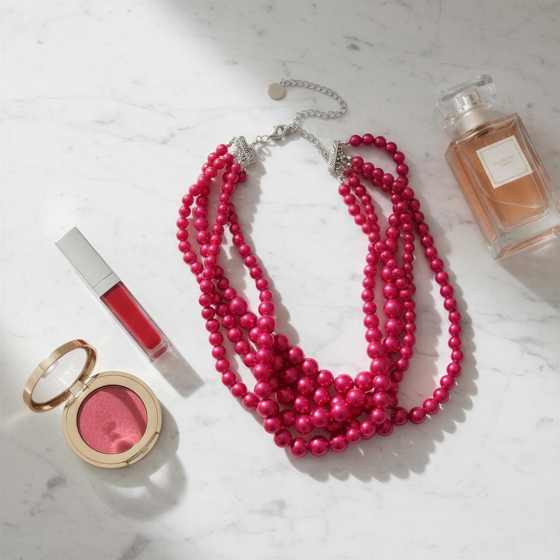 Pink beaded necklace with makeup items on a marble surface