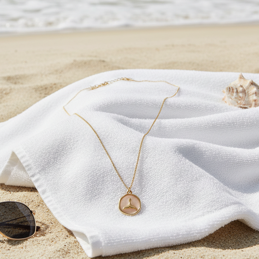 Tidal Embrace Necklace from Chica Chica Jewelry on a white towel with sunglasses on a sandy beach.