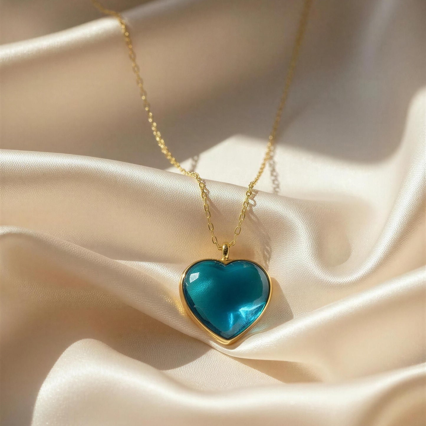 Gold necklace with a blue heart-shaped pendant on a beige fabric background