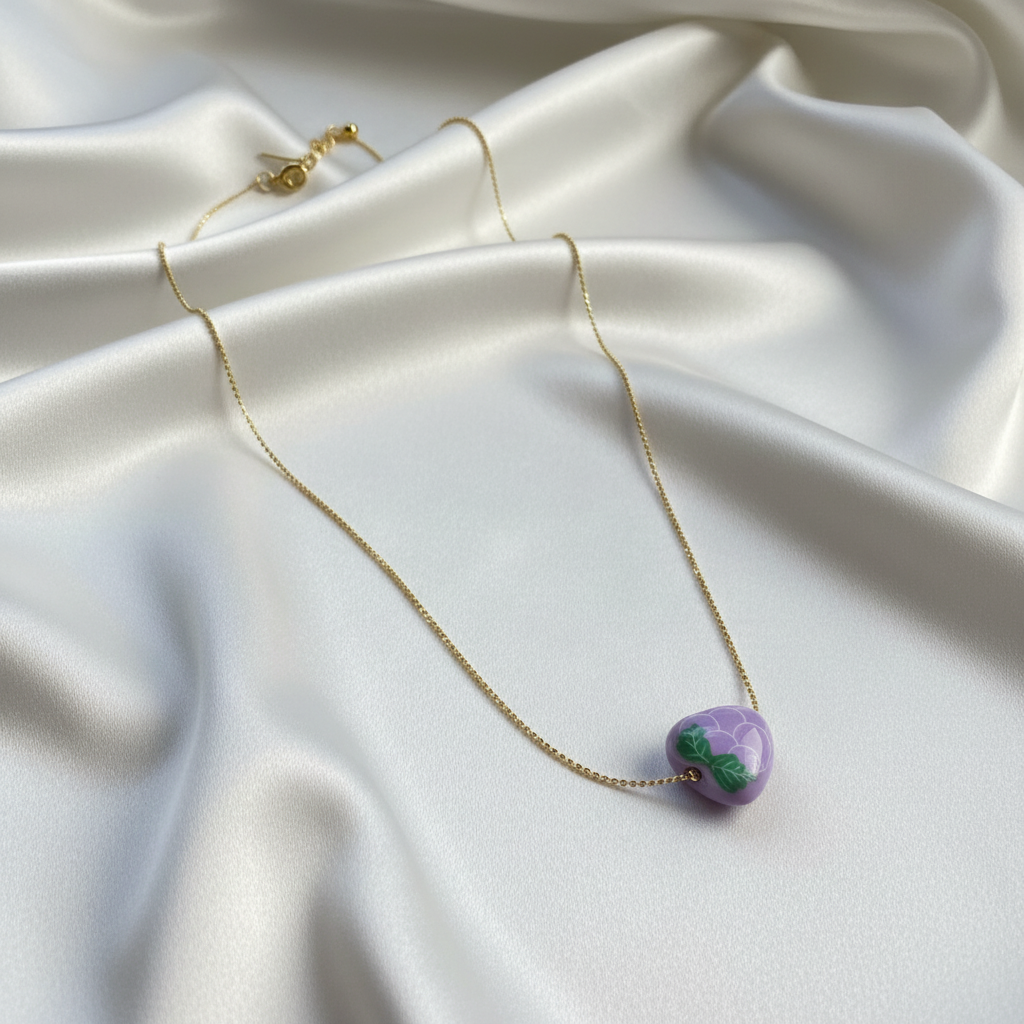 Close-up detail of gold ball chain and grape pendant on soft neutral fabric