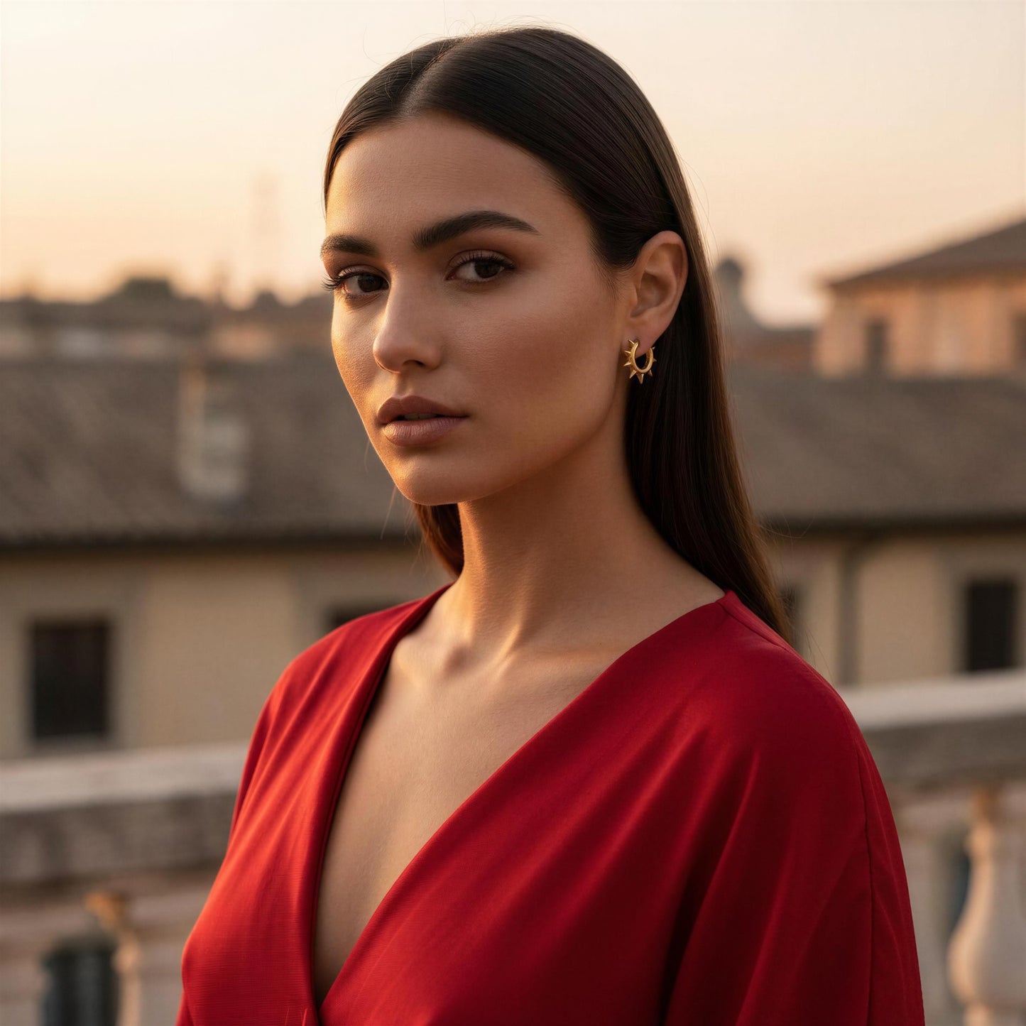 Woman in a red dress standing outdoors with buildings in the background wearing the Valora Spike Hoops