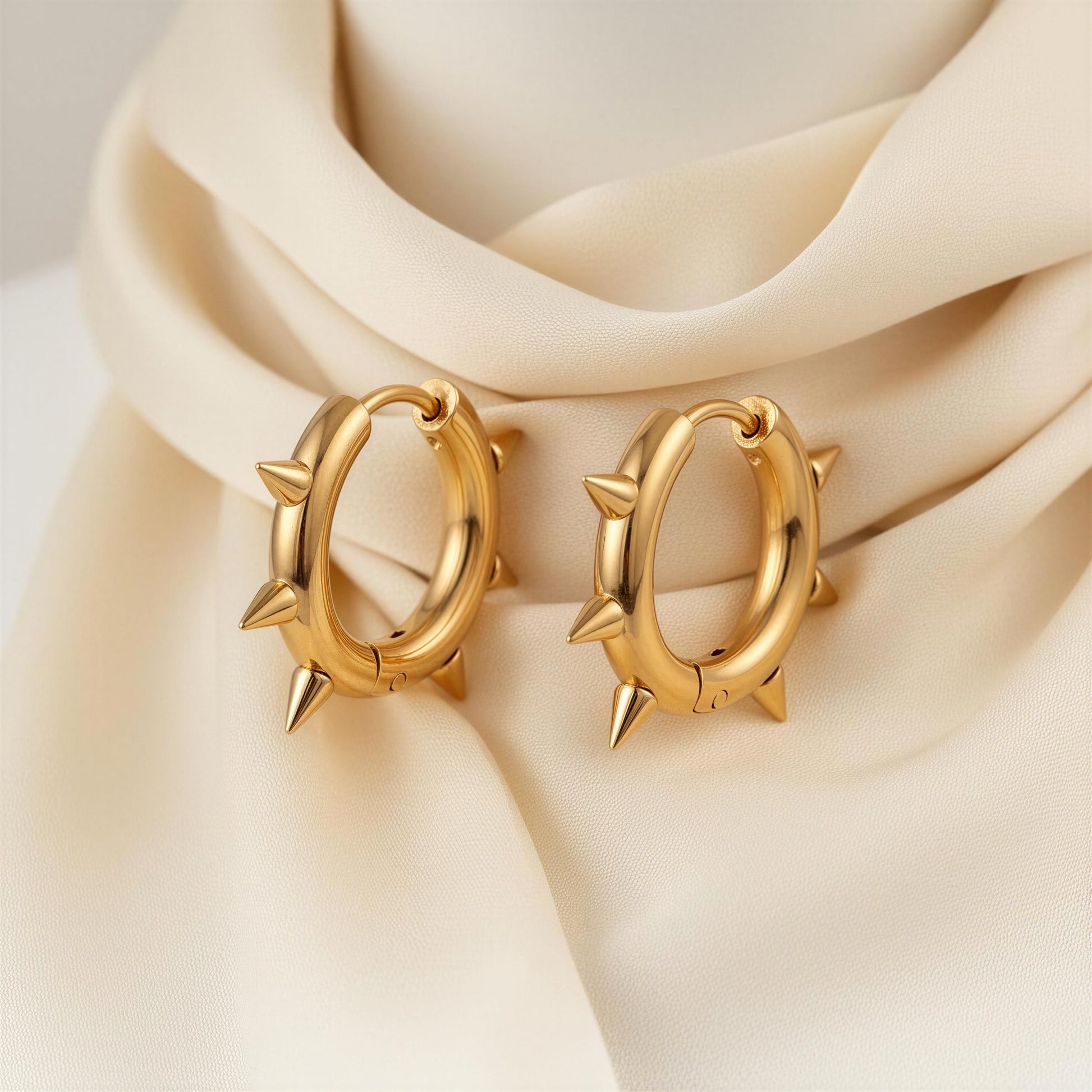 Gold hoop earrings with spike details on a beige fabric background