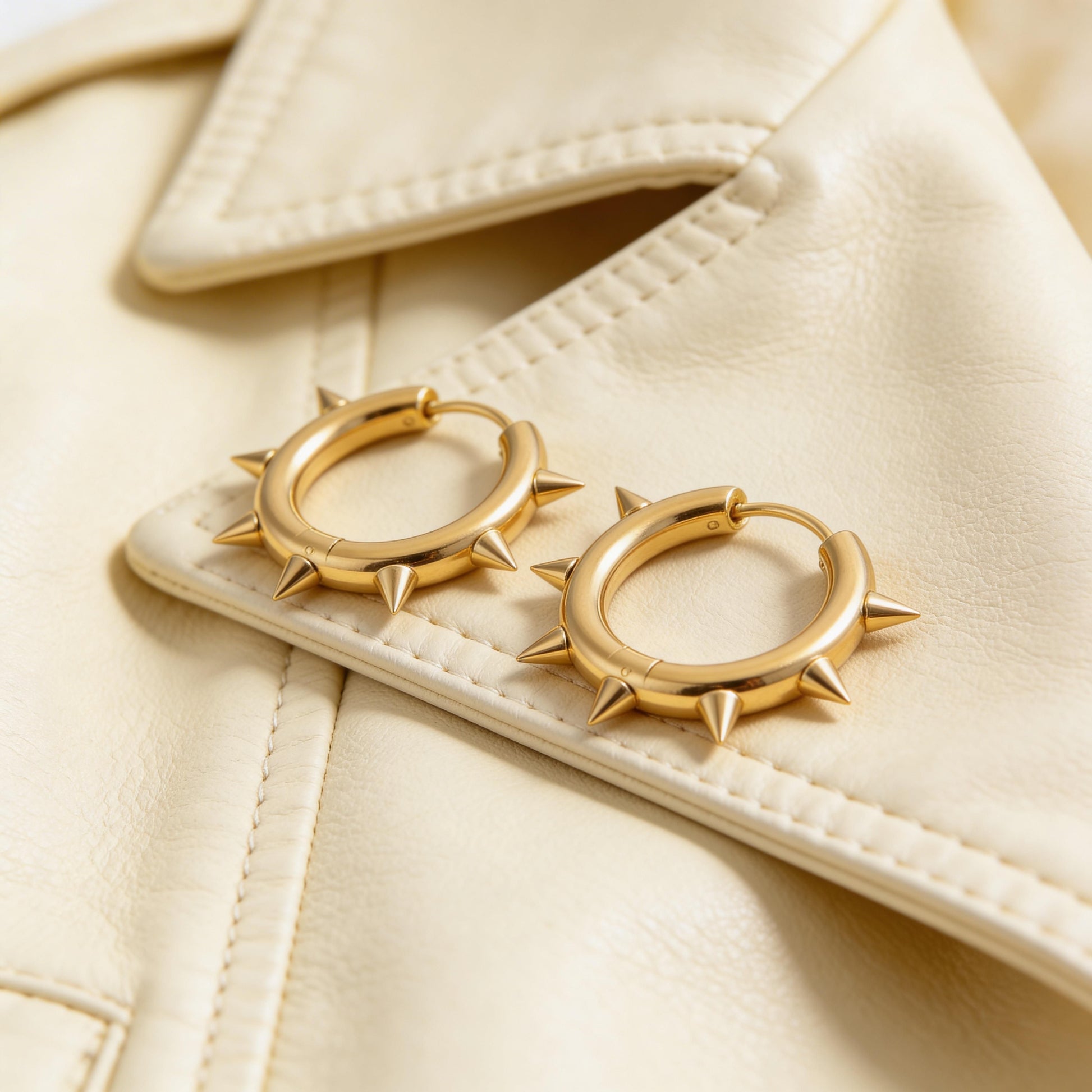 Gold hoop earrings with spike details on a beige jacket