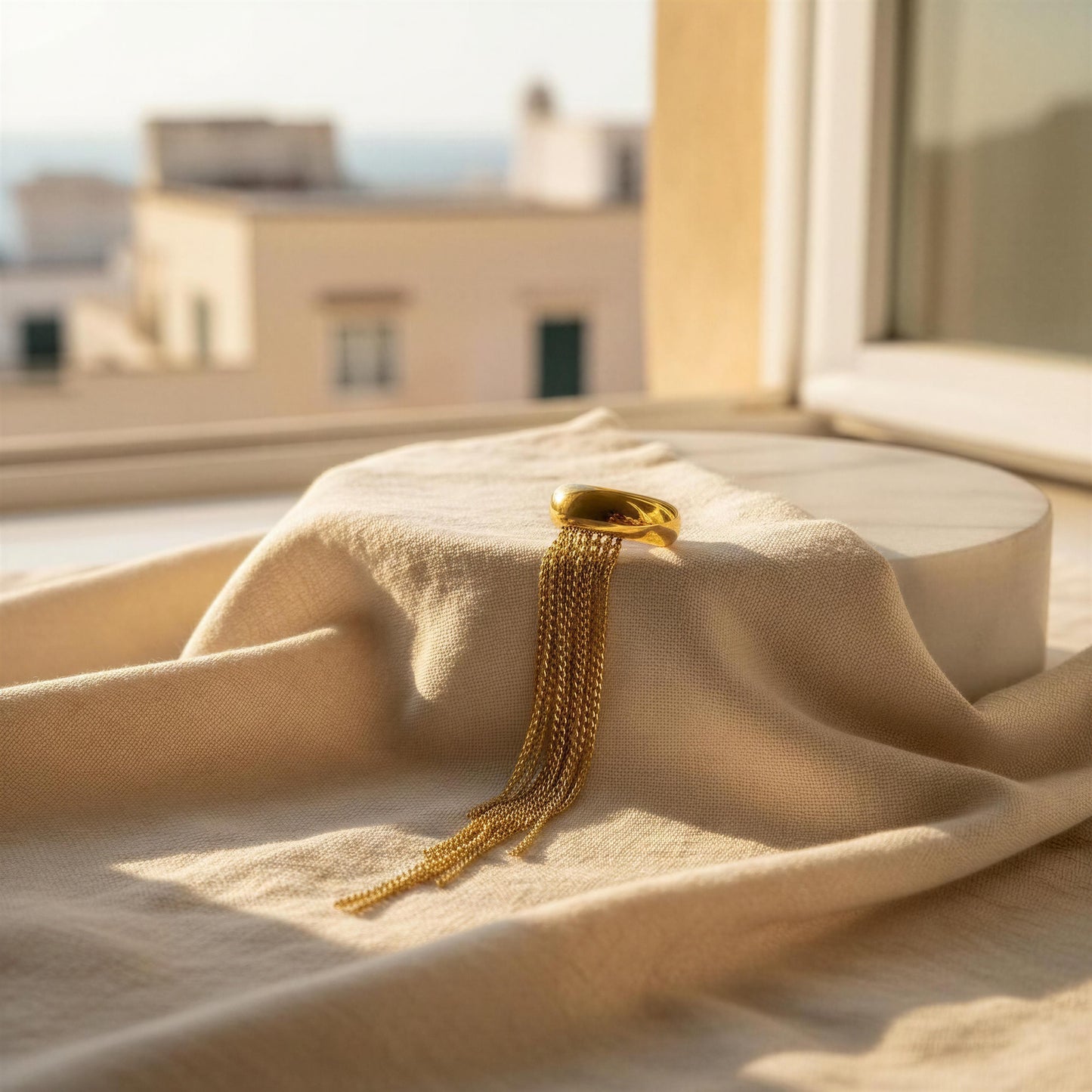 Gold chain necklace on a beige fabric with a blurred architectural background