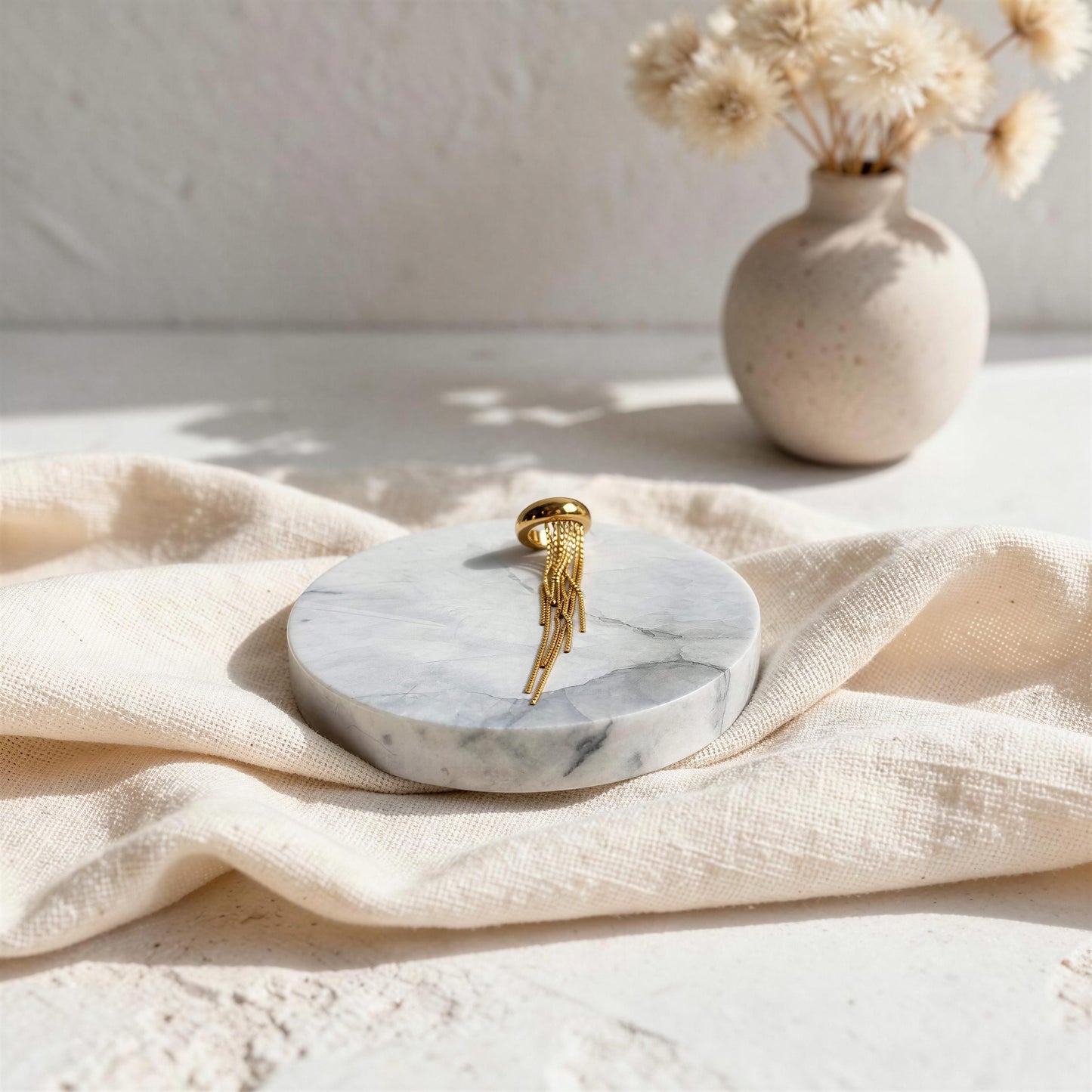 Marble coaster with the Vela Gold Ear Cuff on beige cloth, vase with dried flowers in the background