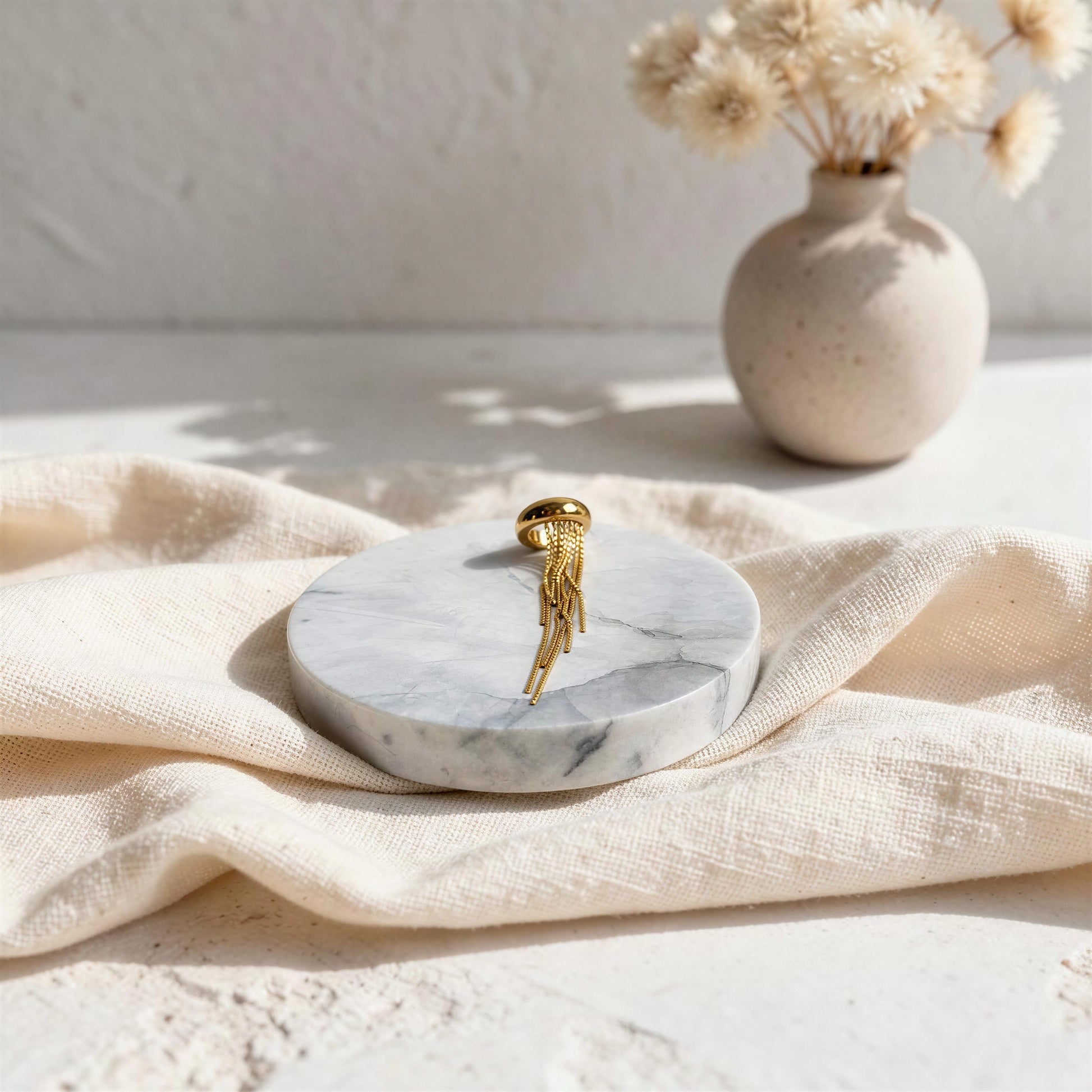 Marble coaster with the Vela Gold Ear Cuff on beige cloth, vase with dried flowers in the background