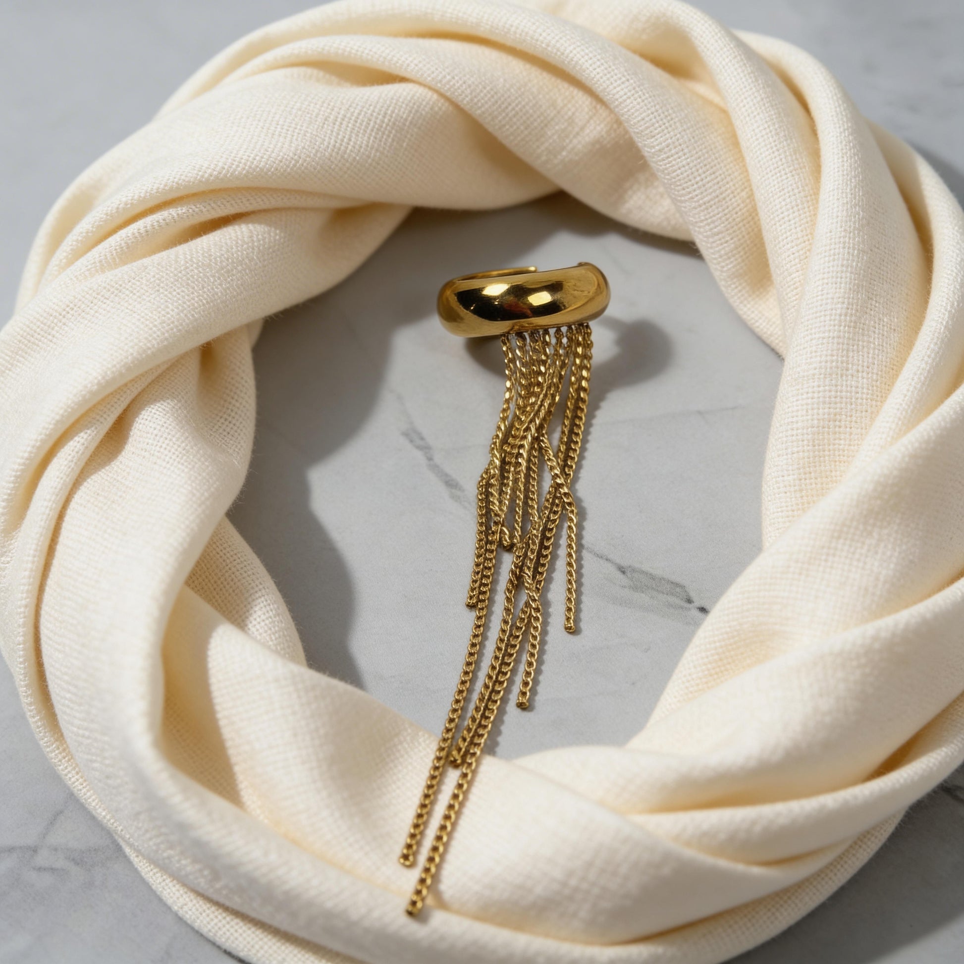 The Vela Gold Ear Cuff on a cream scarf against a marble background