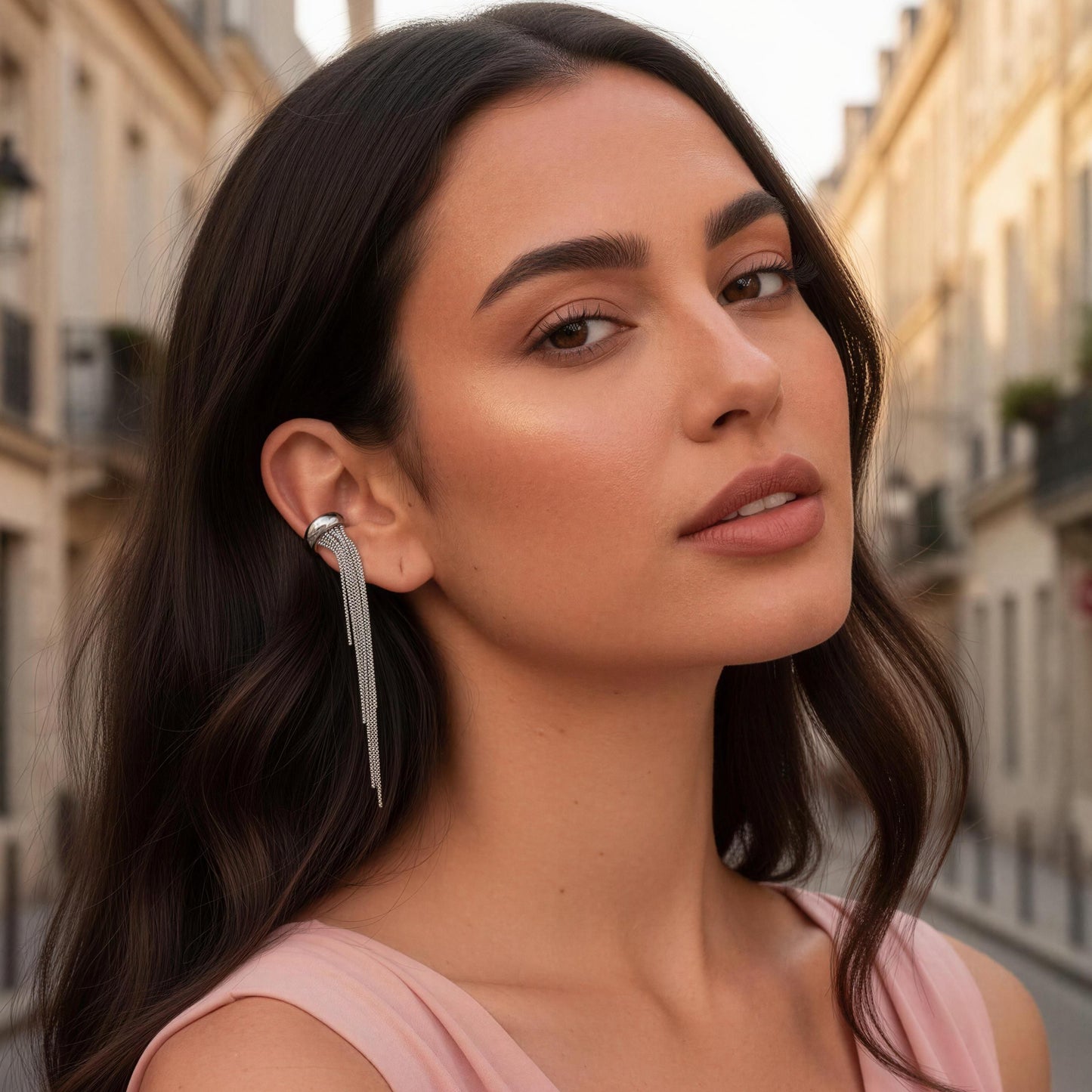 Woman with long dark hair and a pink top standing on a street with buildings in the background wearing the Vela Silver Ear Cuff.
