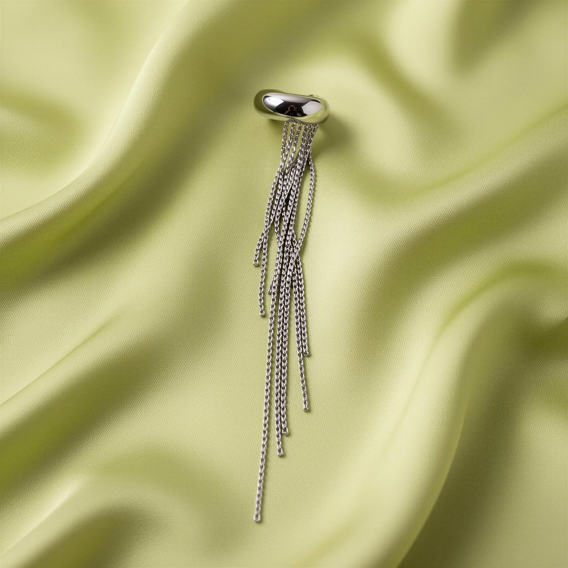The Vela Silver Ear Cuff on a light green satin background