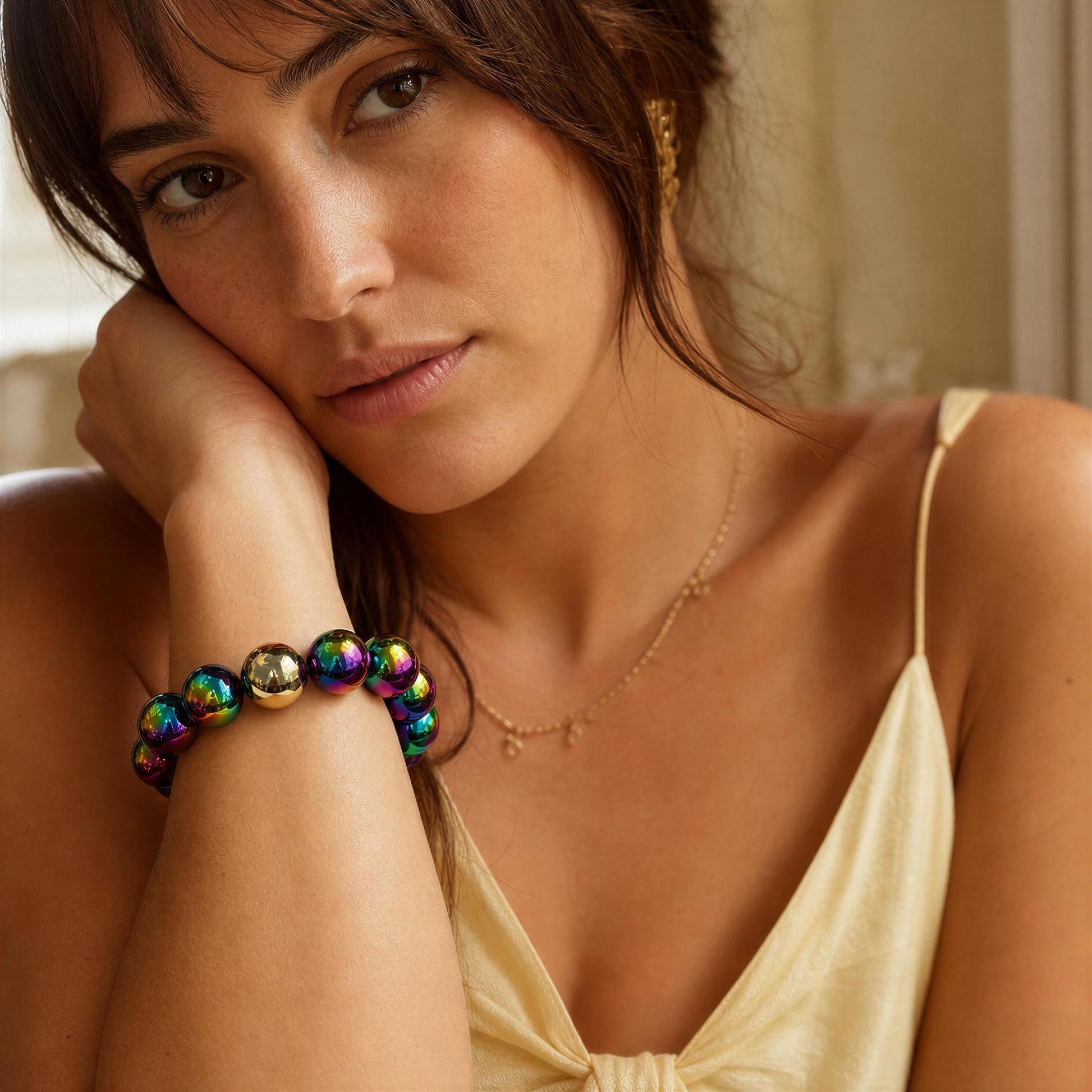 Woman wearing a colorful beaded bracelet and gold necklace, with a neutral background