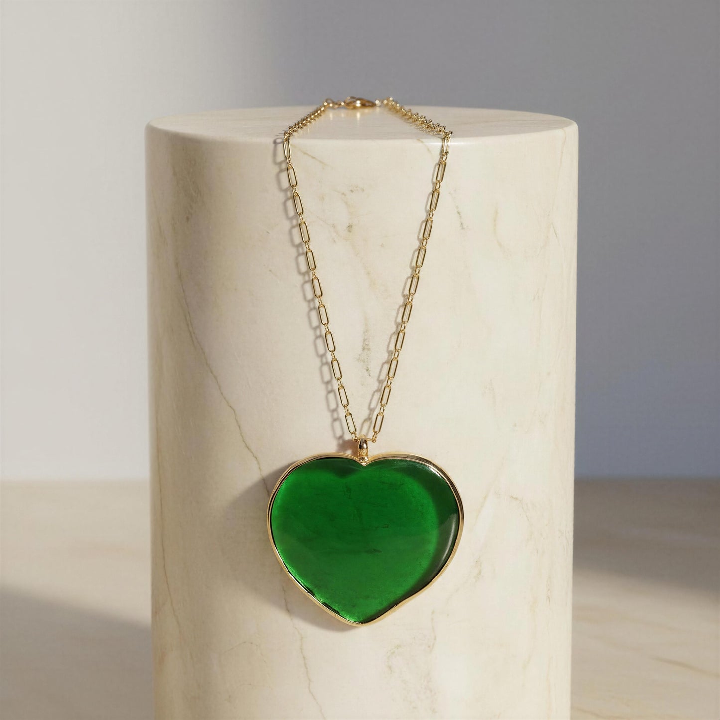 The Verde Murano Heart Necklace on a gold chain against a marble background