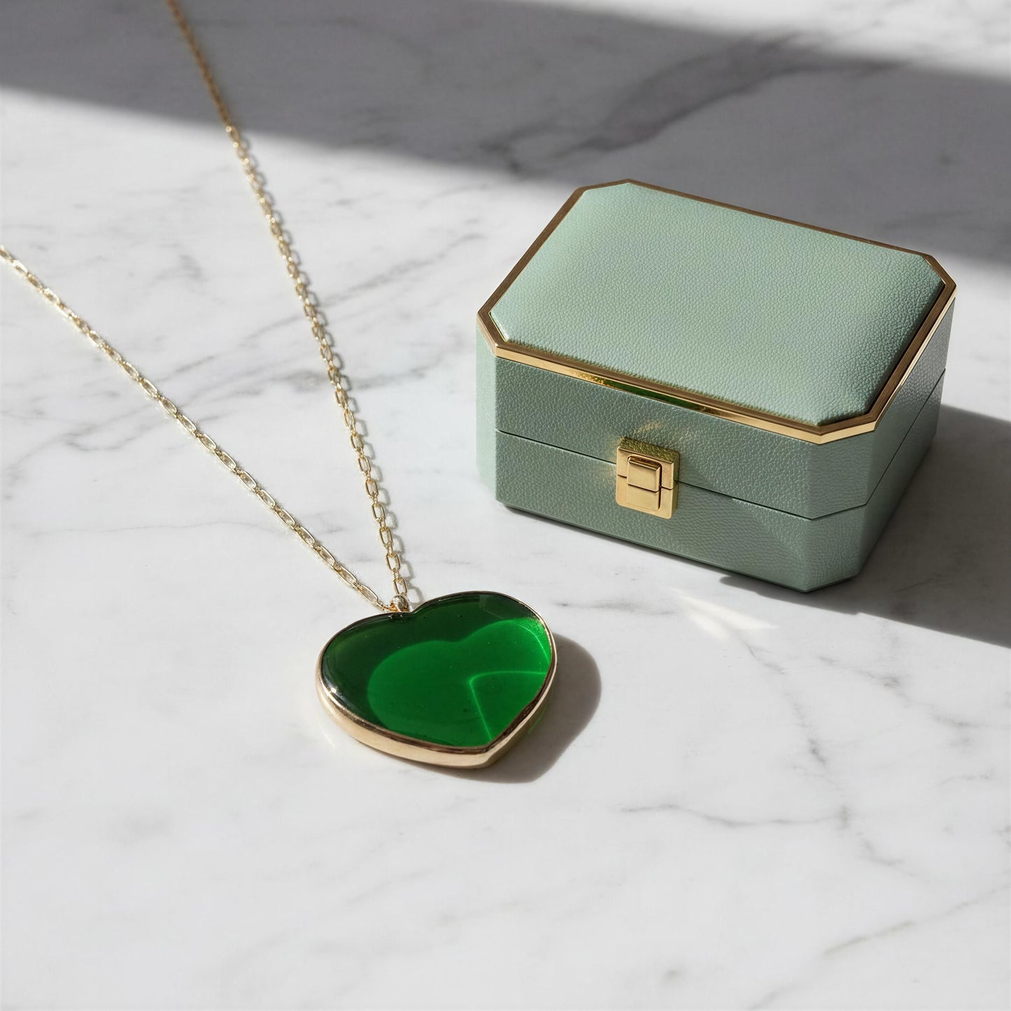 Green heart-shaped pendant necklace on a marble surface with a green jewelry box.