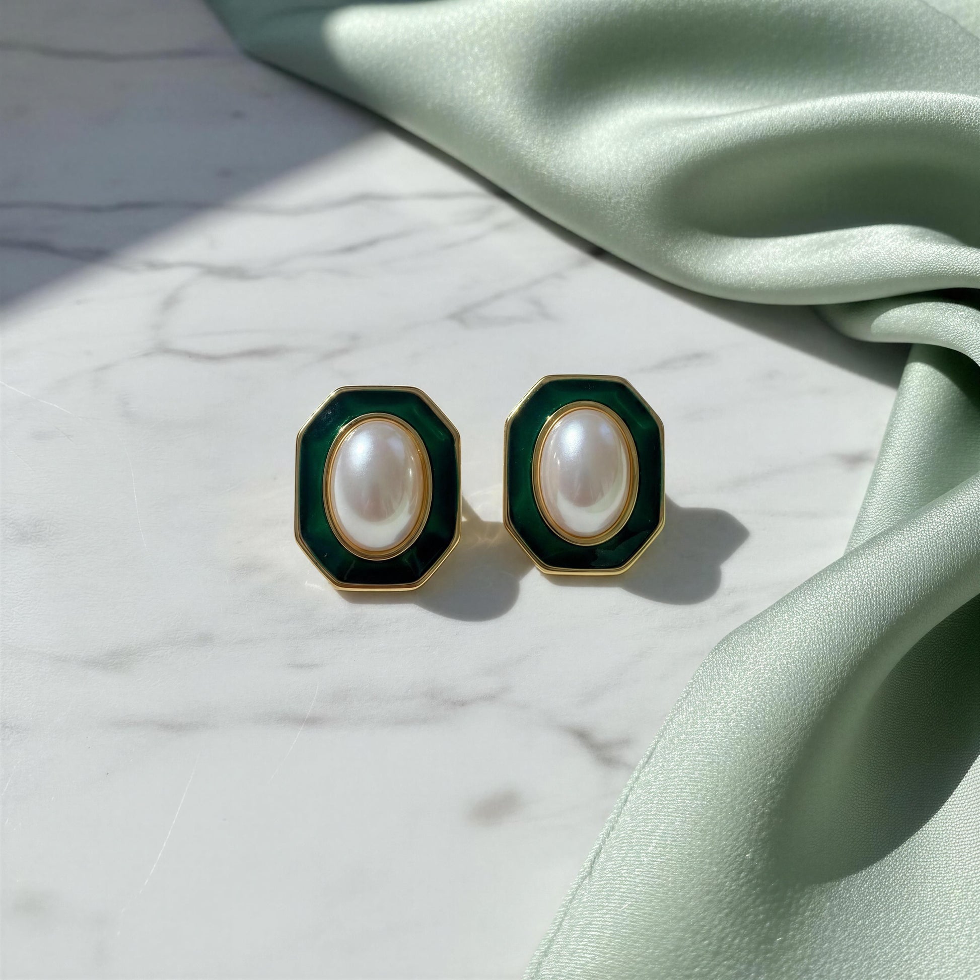 Pair of earrings with green and gold accents on a marble surface with green fabric.