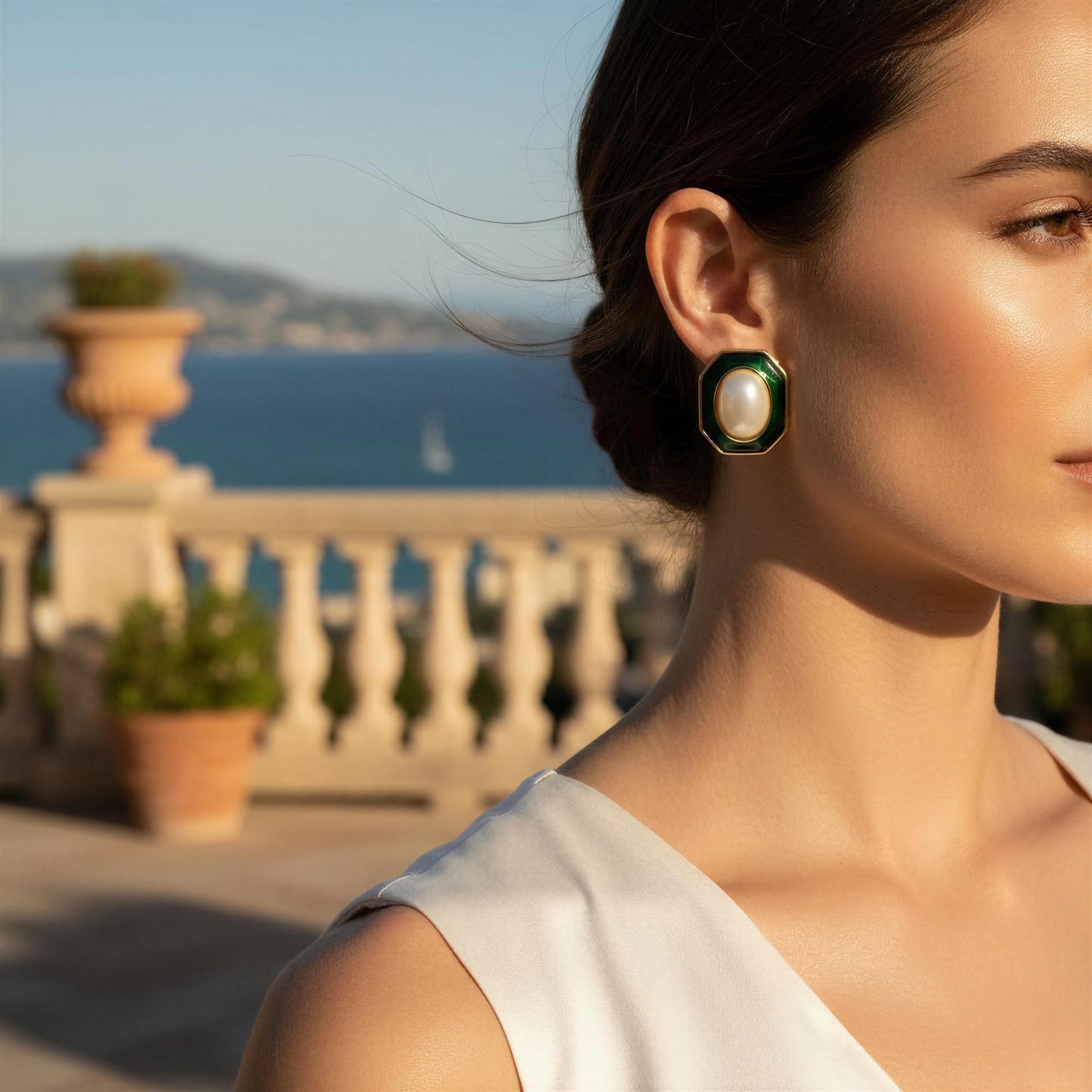 Woman wearing a pearl earring with a scenic background of ocean and mountains.