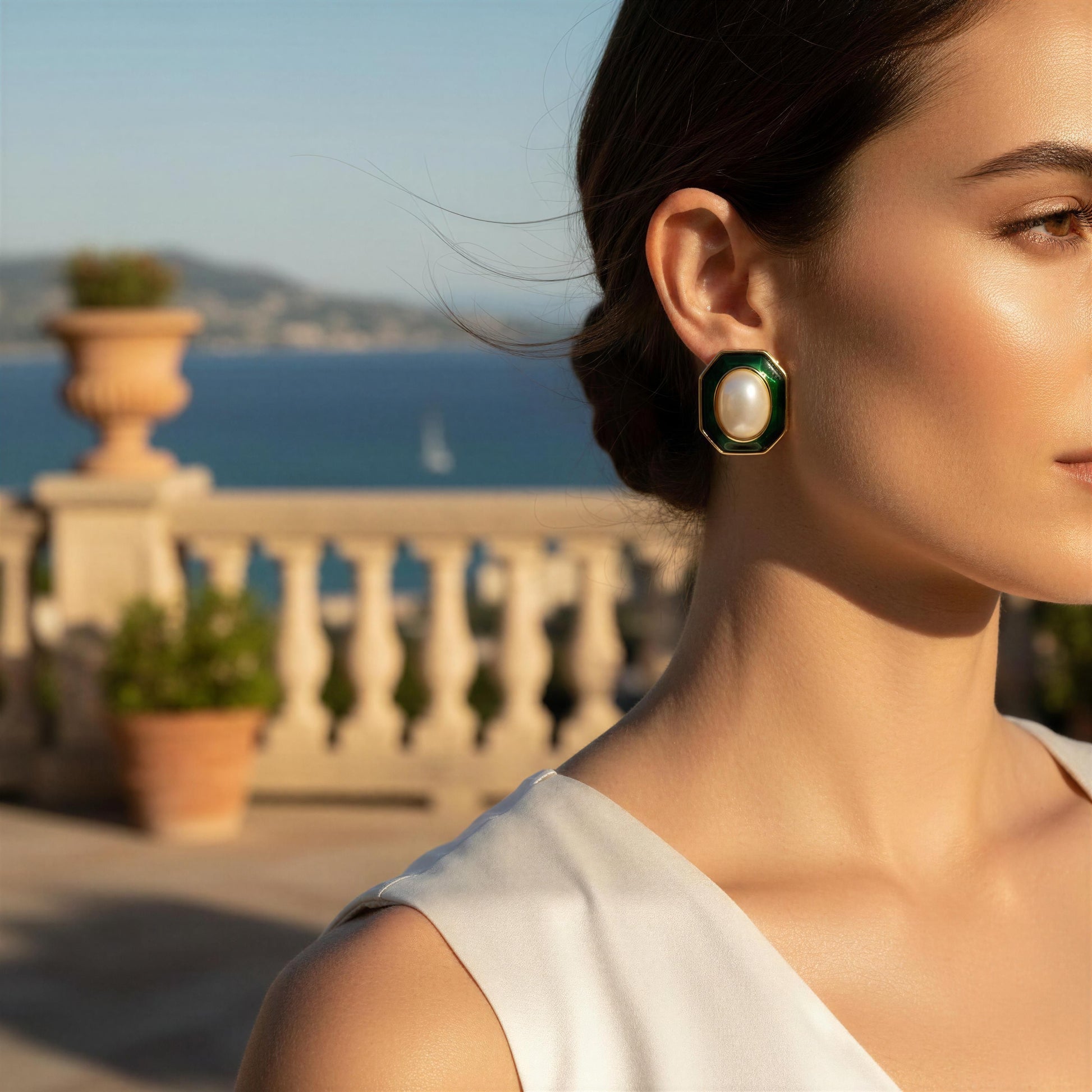 Woman wearing a pearl earring with a scenic background of ocean and mountains.