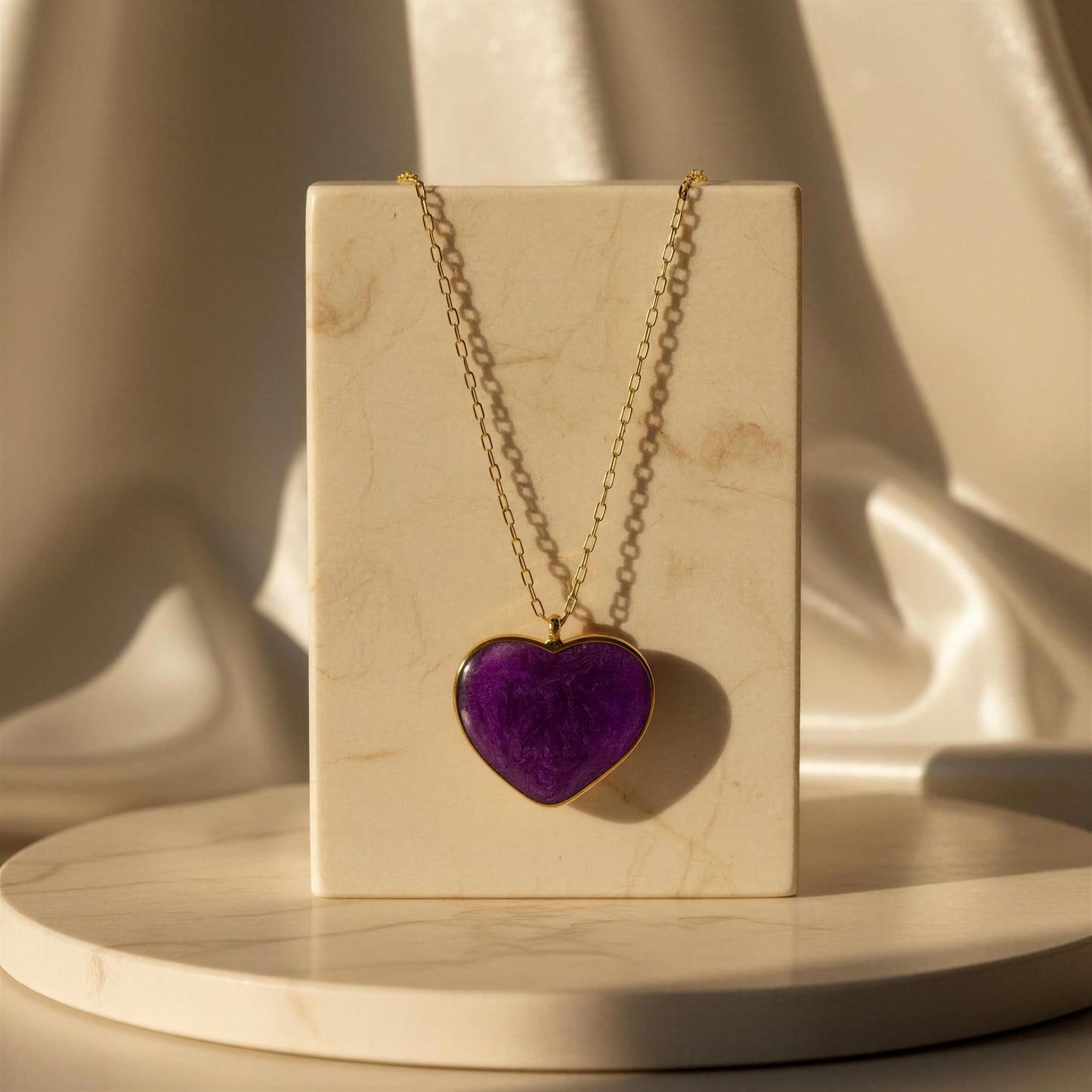 The Viola_Heart_Necklace hanging from a marble pedestal.