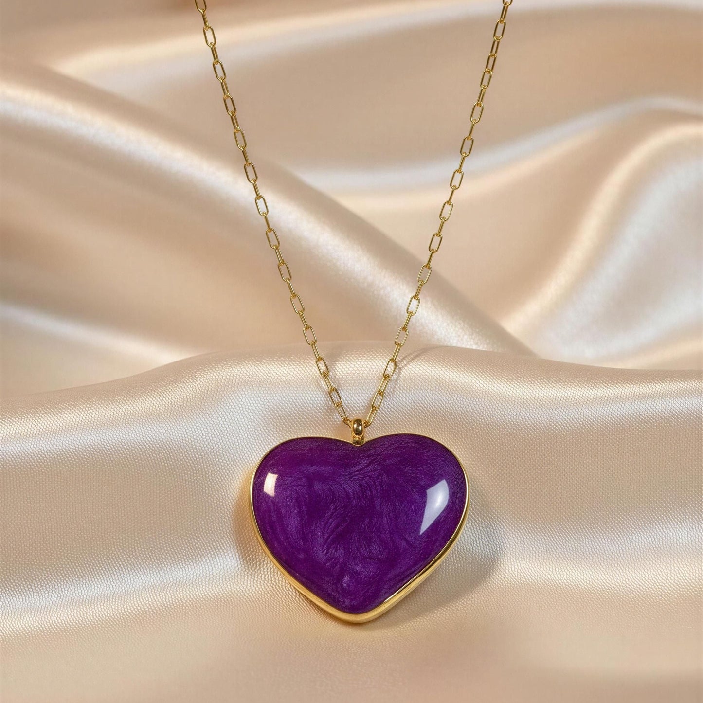 Purple heart-shaped pendant on a gold chain against a beige fabric background