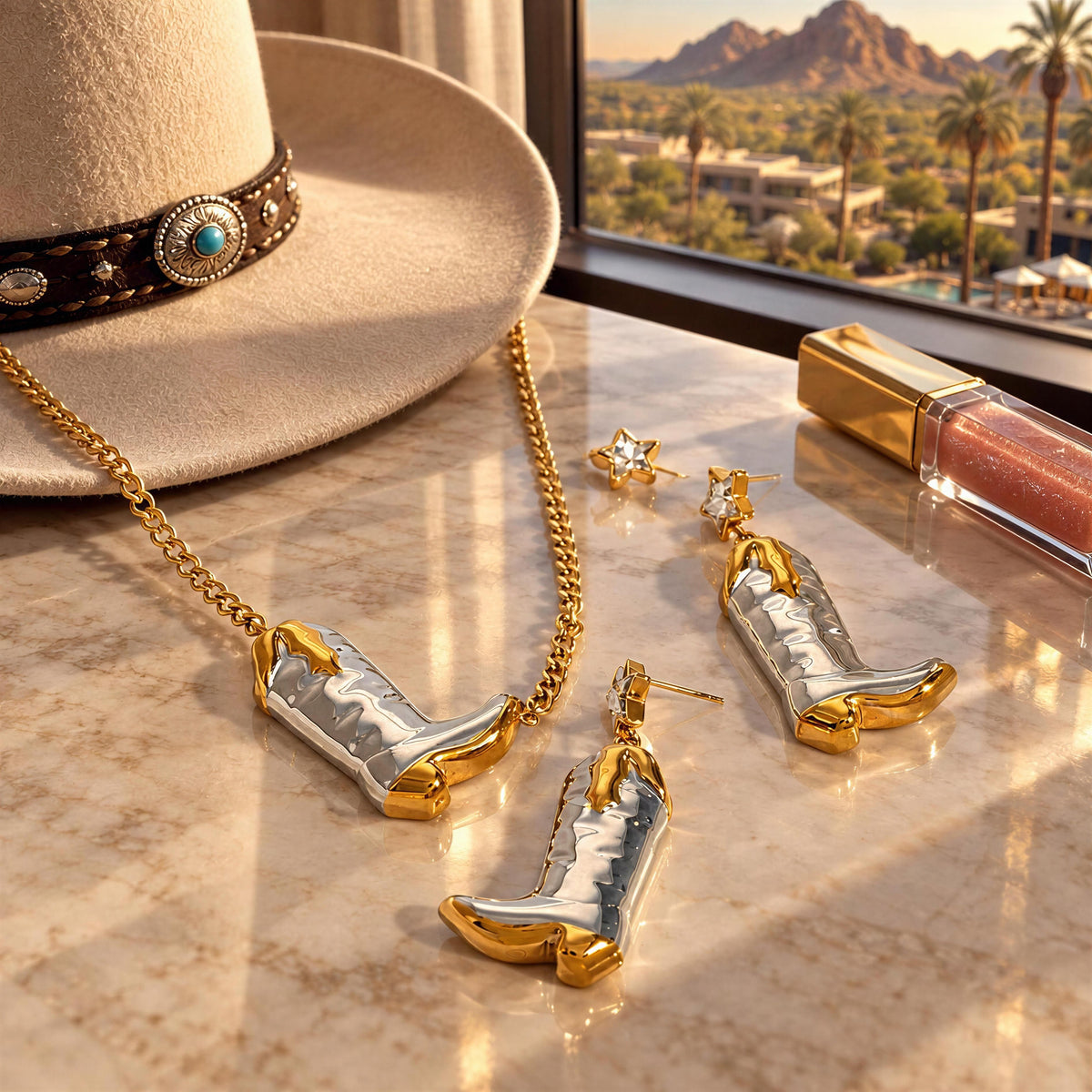 The Frontier Boot Jewelry Set from  Chica Chica Jewelry laying flatlay on marble hotel desk next to a luxury western hat and lipgloss.